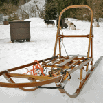 A small wooden toboggan dog sled with a dog sled team in the background
